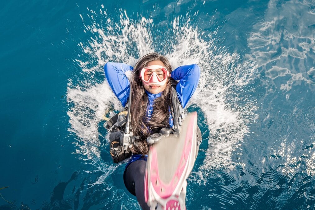 A woman plunges backwards into water with scuba gear on.