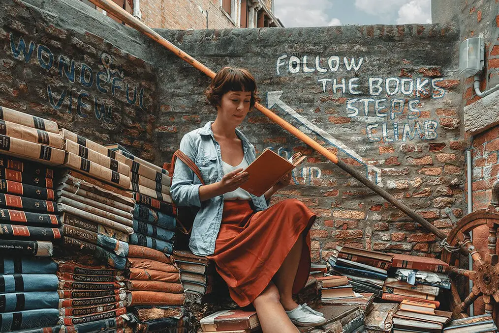 Una persona sentada en una escalera rodeada de libros.
