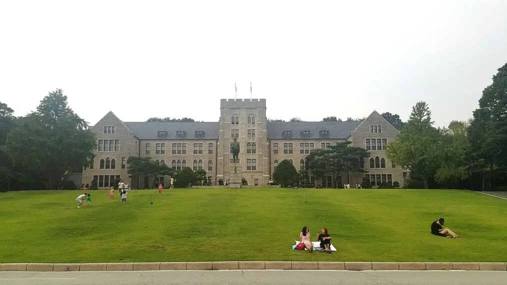 La gente se sienta en el césped frente a un edificio en el campus de la Universidad de Corea.