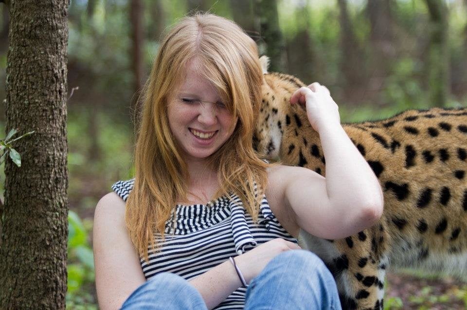 Woman smiles as she pets a cheetah behind her back.