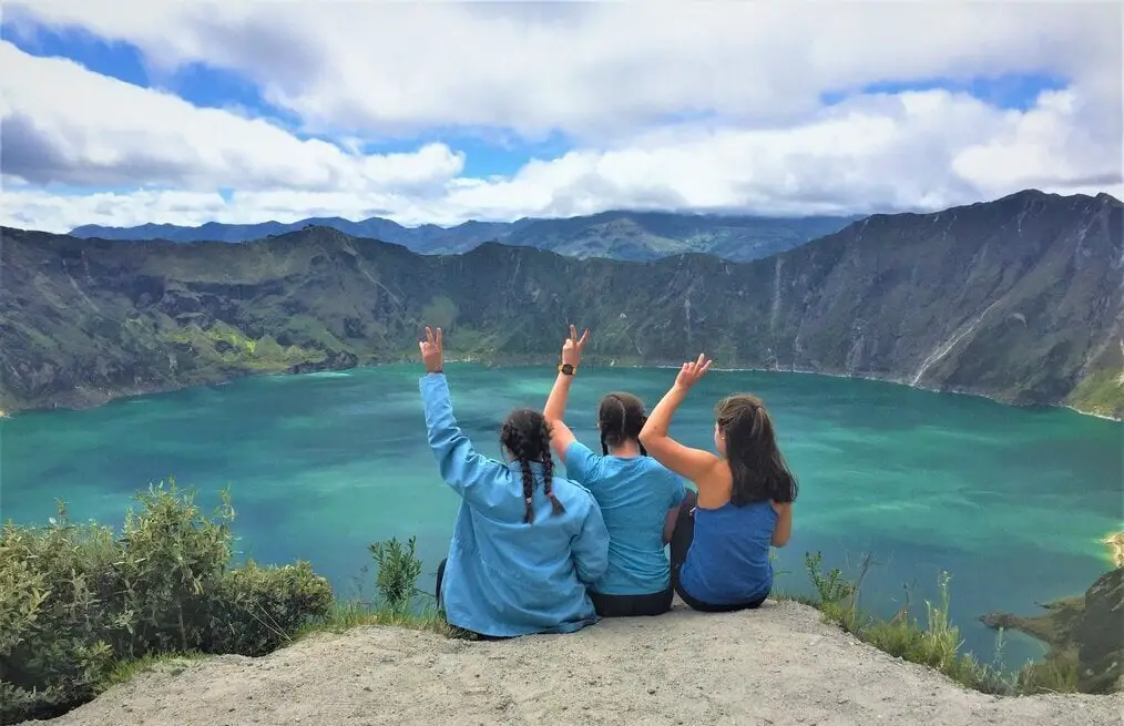 Tres chicas haciendo señales de paz con vistas a la montaña y al lago.
